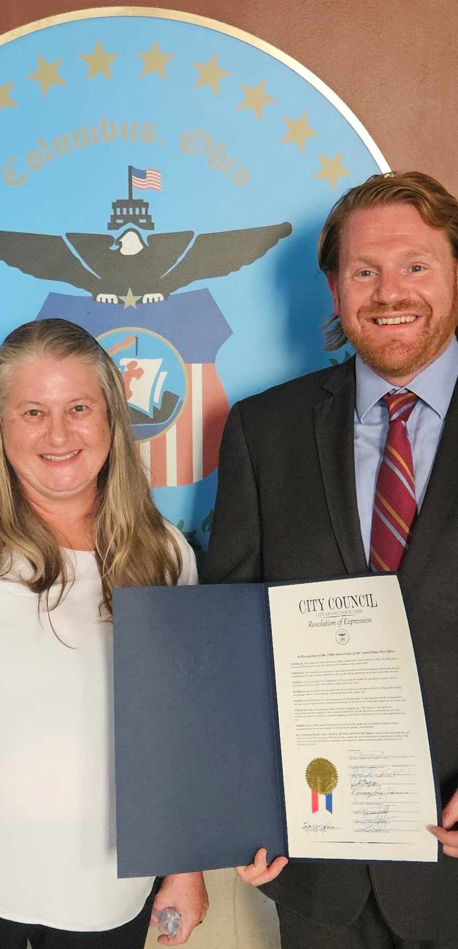 A photo of Columbus Auxiliary Treasurer Angela Lyshe with President Pro Tempore Rob Dorans of the Columbus City Council holding up the signed proclamation